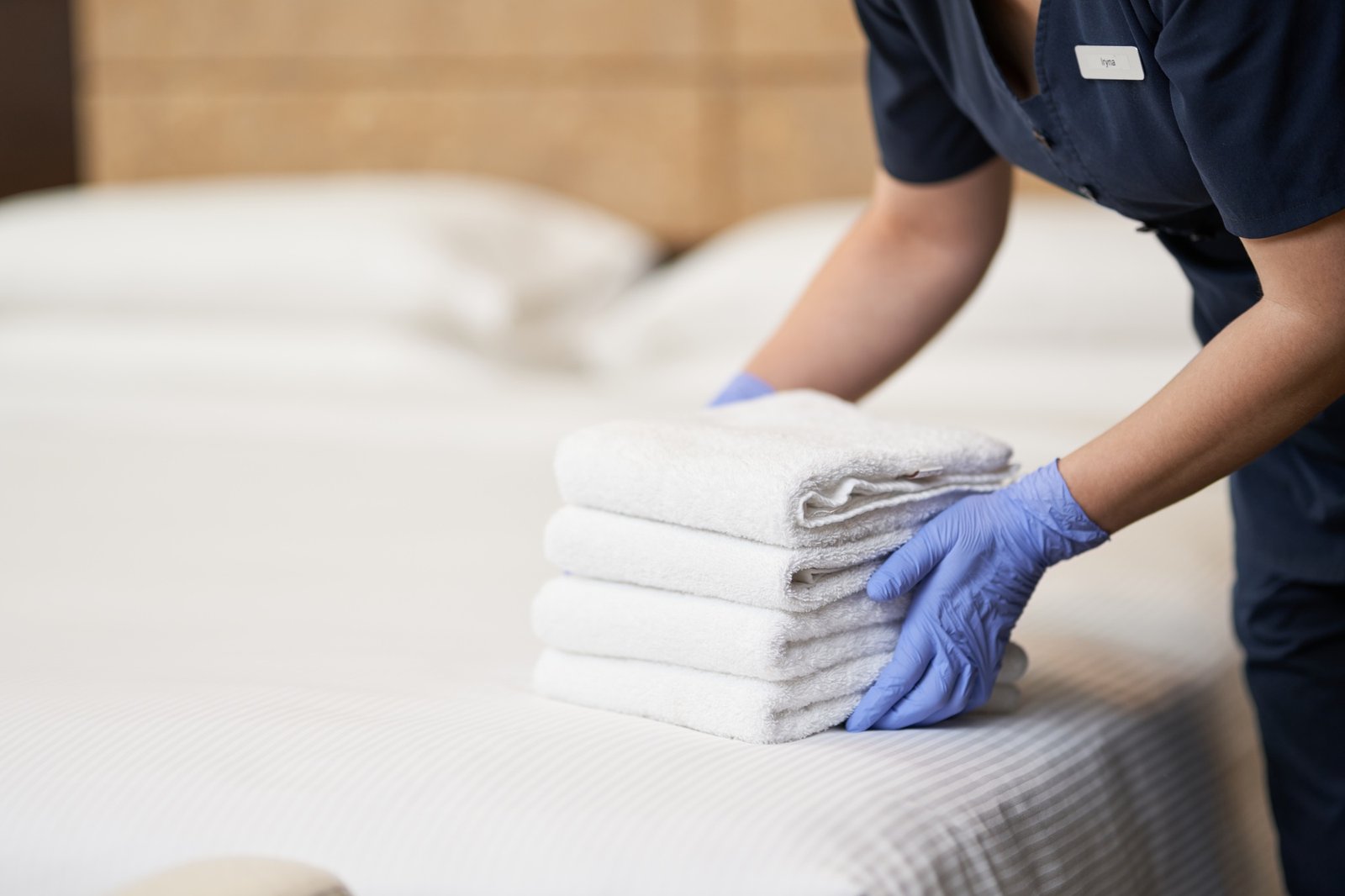 Housemaid making bed in hotel room while folding towels